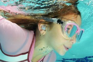 A girl swims underwater with ear plugs.