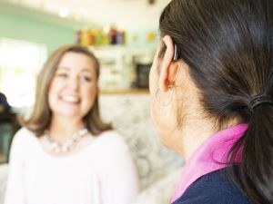 A woman wearing a hearing aid talks happily to a friend. 