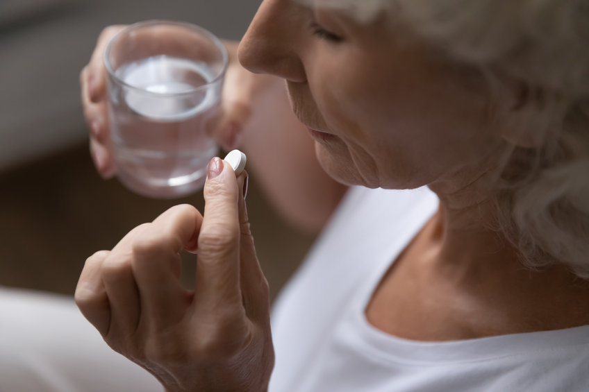 A woman swallows a pill while holding a glass of water. 