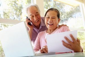 smiling couple talking on phone in front of computer