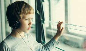 A boy with headphones on looks out the window.