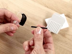 A person cleans their hearing aids using tiny tools.