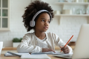 A little girl wearing headphones sits at her computer doing schoolwork.