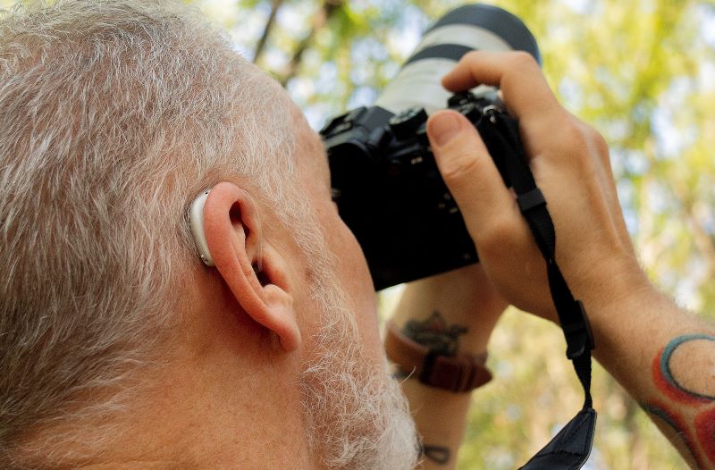 A birder uses his camera while wearing hearing aids. 