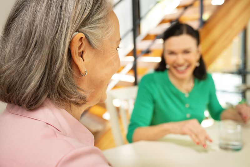 A woman with a hearing aid chats with her friend. They are happy to be able to understand each other. 