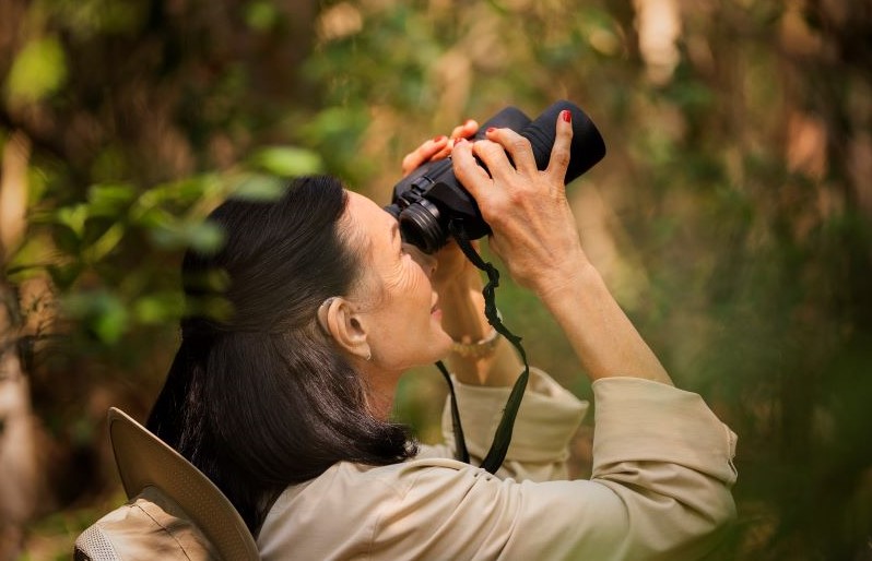 A woman with hearing aids looks for birds with a binocular.