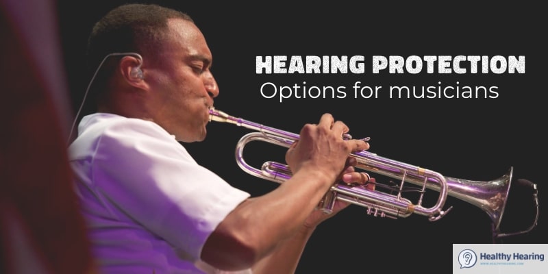 A man blows a trumpet while wearing in-ear monitors.