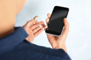 A hearing aid and a smartphone, held by a man.