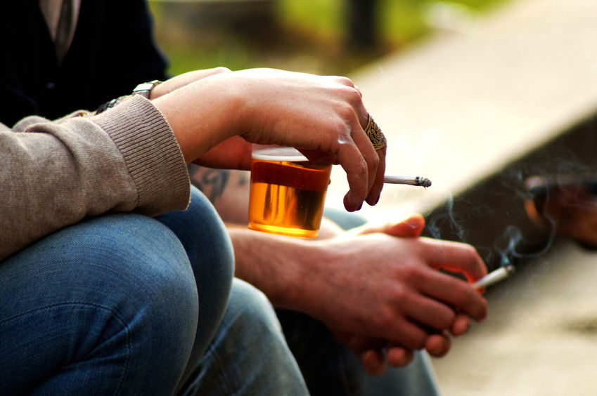 A person holding a drink and a cigarette. 
