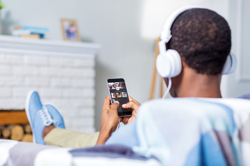 A man wears headphones and looks at his phone.