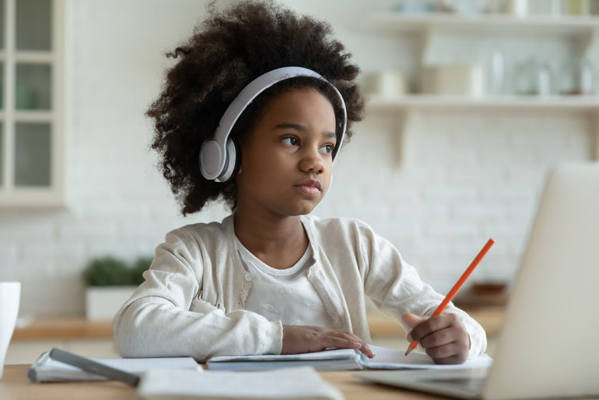 A little girl wears headphones as she completes schoolwork.