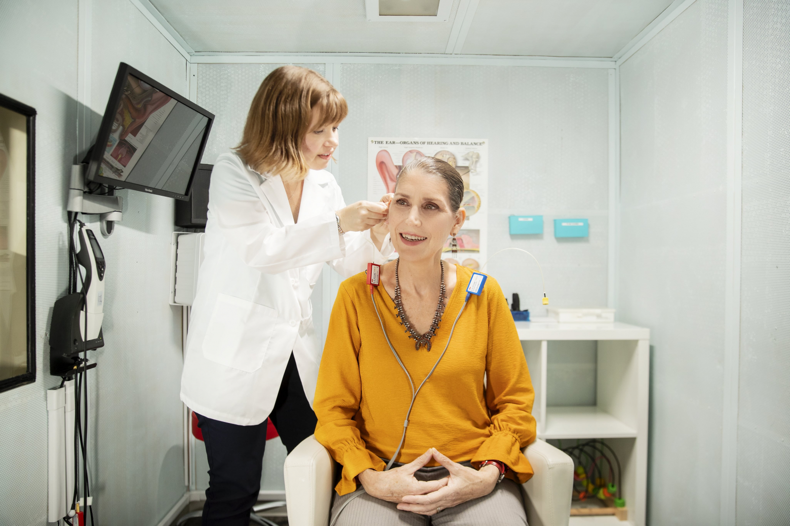 A woman receives a hearing exam in a hearing test booth.