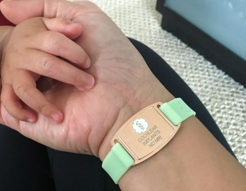 A wrist with a medical ID bracelet indicating cochlear implants and no MRIs.