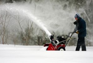 Man bundled up for winter and pushing a snowblower